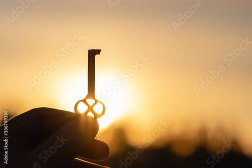 A man holds an old beautiful key in bright sunlight with his hand. Close-up with blurred background.