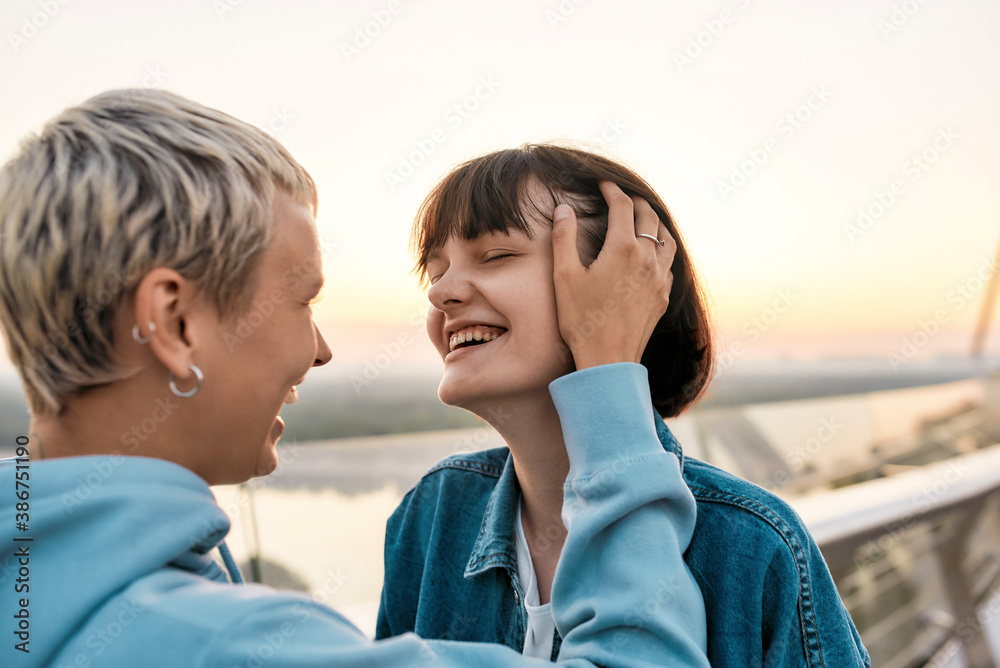 Close up of young sensual lesbian couple laughing, enjoying romantic moments while standing on the bridge together at sunrise Close up of young sensual lesbian couple laughing, enjoying romantic moments while standing on the bridge together at sunrise