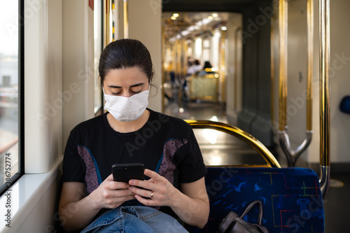 A young girl in a black mask looking at her smart phone while traveling in the subway photo