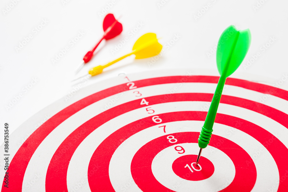 Close-up of a bull's eye on a wall with three Darts, one dart hits the target, the others lie side by side Close-up of a bull's eye on a wall with three Darts, one dart hits the target, the others lie side by side