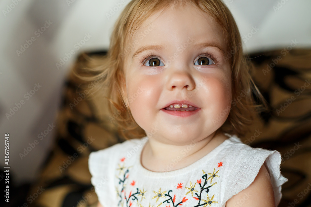 A 2 years old girl is sitting on the bed and smiling. The child rejoices and turns over. Happy child A 2 years old girl is sitting on the bed and smiling. The child rejoices and turns over. Happy child