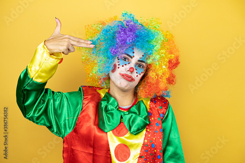 Clown standing over yellow insolated yellow background Shooting and killing oneself pointing hand and fingers to head like gun, suicide gesture.