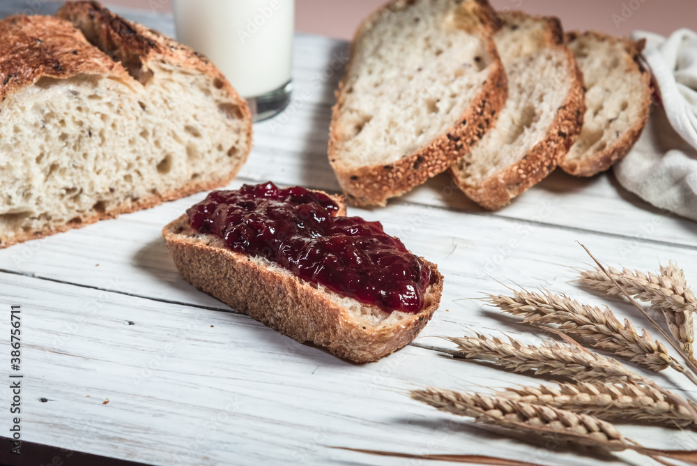 A glass of milk, sliced rustic bread and jam, on a white wooden board. Healthy food and farming concept