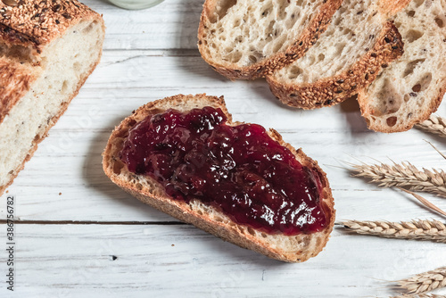 A slice of rustic bread smeared with jam on a white wooden board. Healthy food and farming concept
