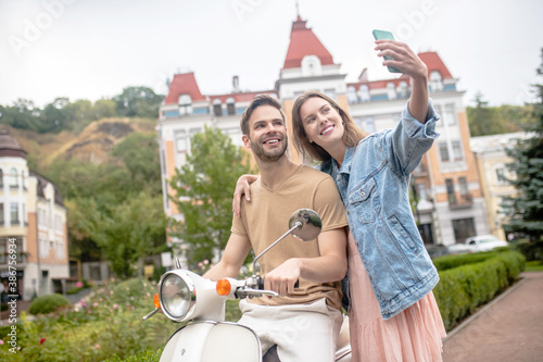 Woman taking a selfie with her boyfriend and a scooter