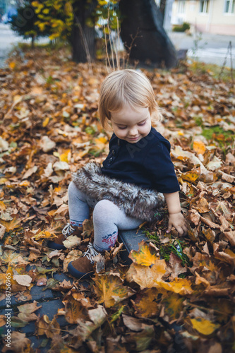 A little girl of 1.5 years is standing and smiling. The child throws leaves. Cheerful girl in the autumn forest