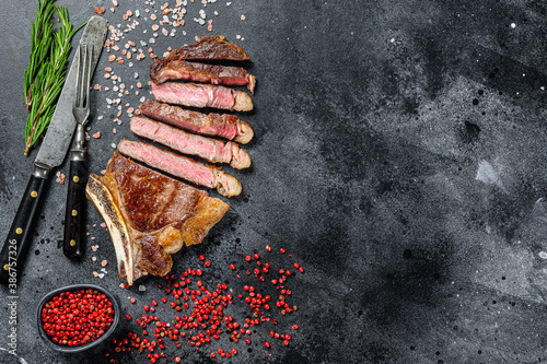Ribeye steak on the bone with salt and pepper. Grilled Beef meat.  Black background. Top view. Copy space