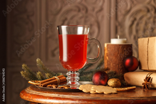 The concept of the winter holidays. Mulled wine in a glass glass, on a copper tray with spices, fir branches. On a vintage wooden table with gifts. Close-up, low key