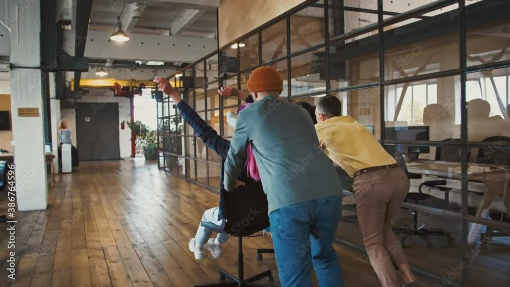 Chair race competition. Cheerful millennials riding on office furniture, having fun at work, slow motion Chair race competition. Cheerful millennials riding on office furniture, having fun at work, slow motion