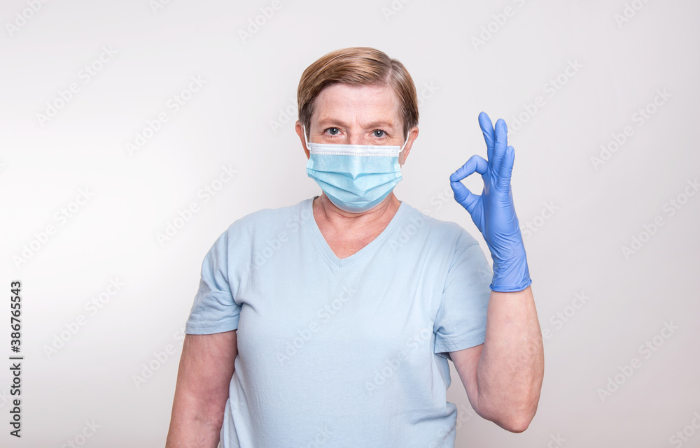 Elderly woman wearing mask and gloves and showing ok sign