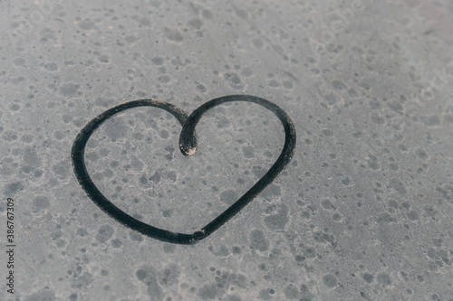 Heart symbol on dirty car window. Heart drawn with a finger on the glare side window of a car. Finger-painted heart. Valentine's Day romantic drawing. A car that hasn't been washed for a long time.