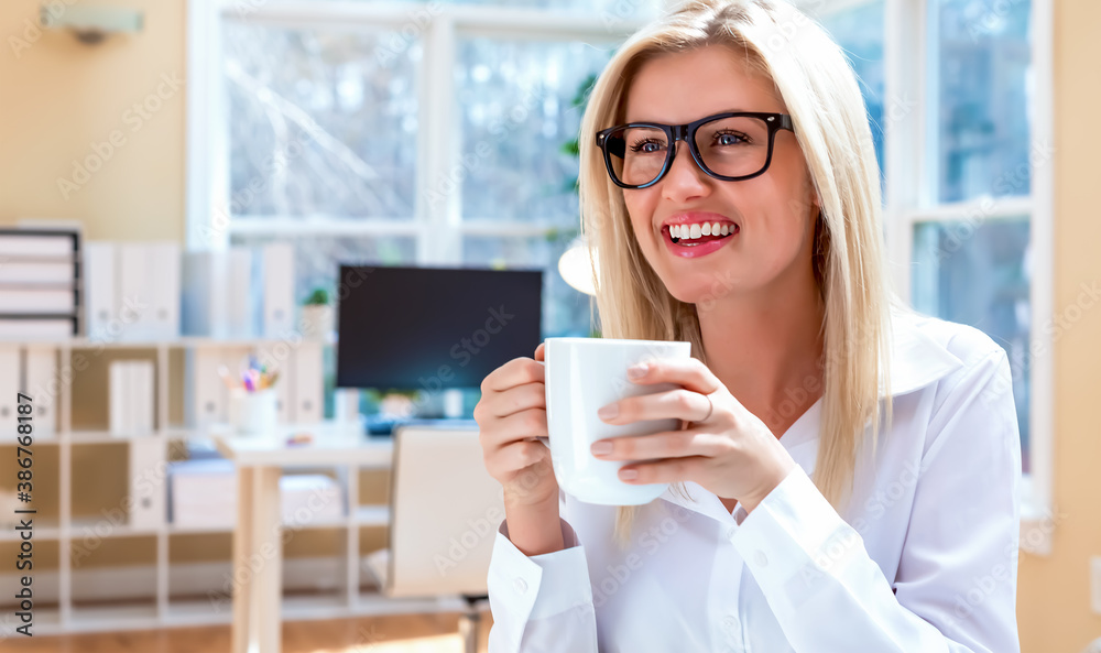 Happy young woman drinking coffee in her home office Happy young woman drinking coffee in her home office