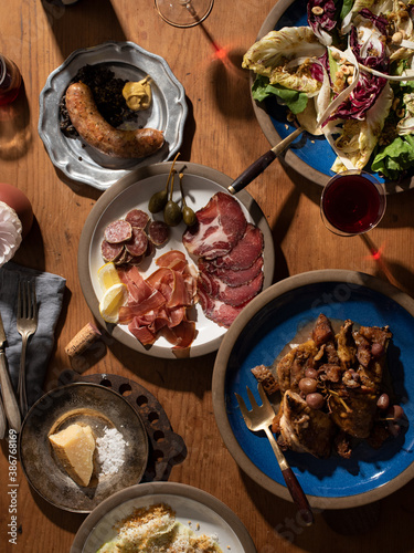 Top down of a dinner feast with many plates of salad, sausage, chicken, meats