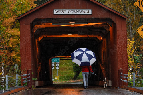 West Cornwall, Ct, USA  A woman with an umbrella walks her dog near the covered bridge in the rain. photo