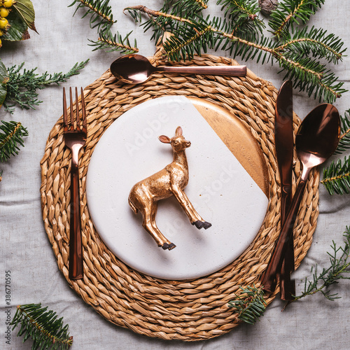 Elegant Christmas place settings with natural branches decoration and golden plate. Reindeer figurine on the dish on wood table background photo