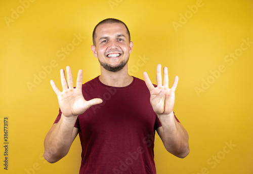 Russian man wearing basic red t-shirt over yellow insolated background showing and pointing up with fingers number nine while smiling confident and happy.