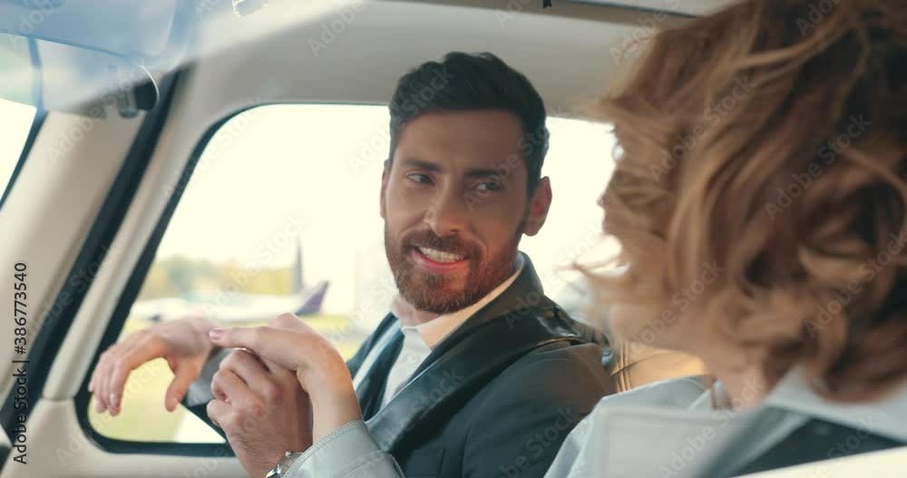 Close up portrait of happy Caucasian handsome bearded man speaking with beautiful young joyful woman while sitting in airplane on set. Male actor kisses female hand and talks. Film industry concept Close up portrait of happy Caucasian handsome bearded man speaking with beautiful young joyful woman while sitting in airplane on set. Male actor kisses female hand and talks. Film industry concept