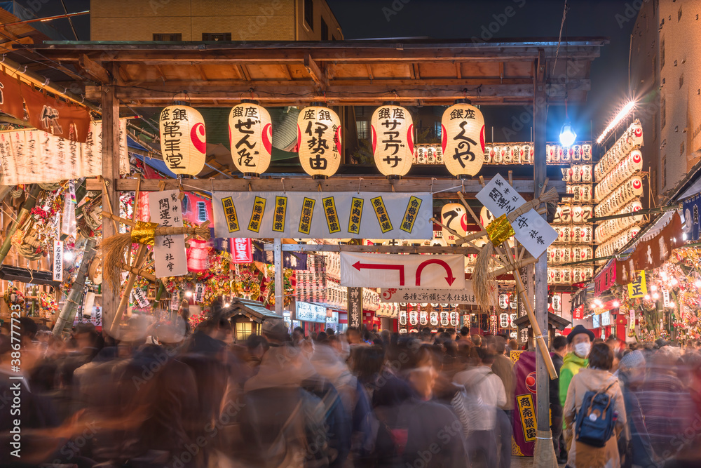 Crowd passing through a gate of Tori-no-Ichi Fair decorated with luminous lanterns in Ootori shrine where traders buy auspicious rakes to have success in business.