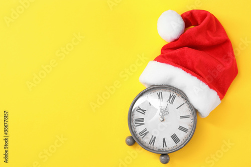 Alarm clock and Santa hat on yellow background, top view with space for text. New Year countdown