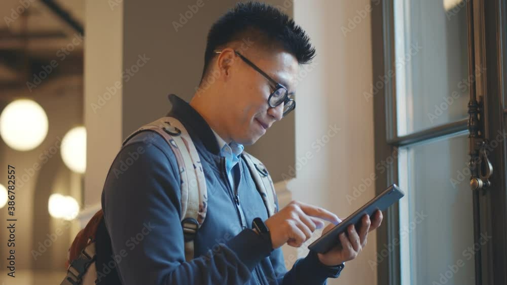 Smiling male college student checking mobile phone in campus building