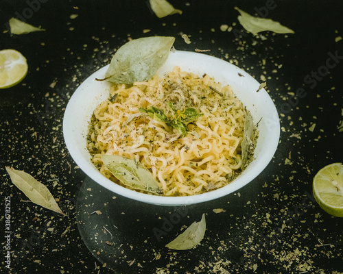 Sopa de fideos en plato blanco minimalista adornada con hojas sobre mesa negra