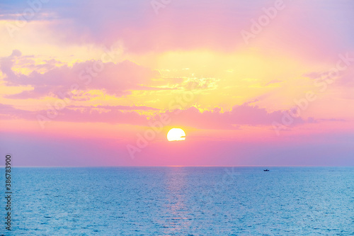 Spectacular beautiful sunset or sunrise on the mediterranean sea. Beautiful pink orange purple yellow light filters through the clouds. A small dinghy boat sails at the horizon on the turquoise sea