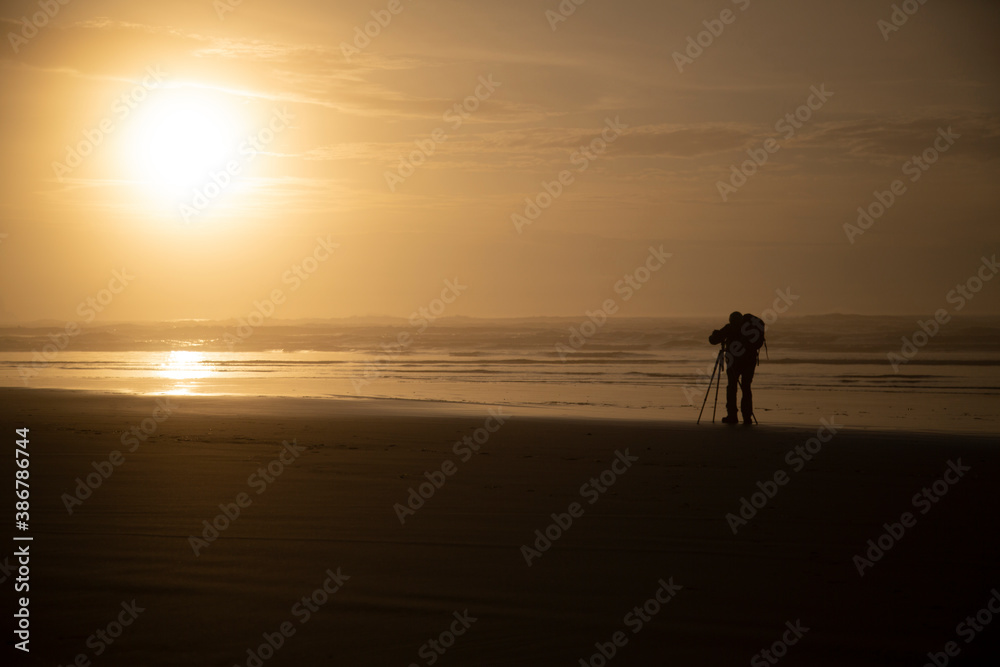 A distant backside view of a photographer on the beach at sunset 
