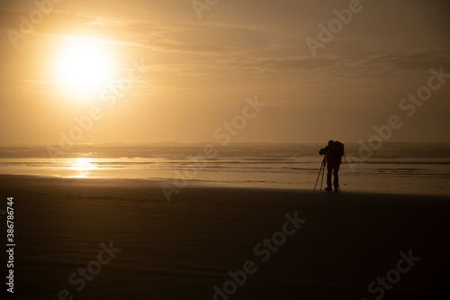 A distant backside view of a photographer on the beach at sunset 