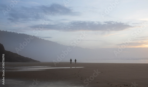 A far off view of two people walking on a foggy beach at sunset - Cape Lookout Beach, Oregon 