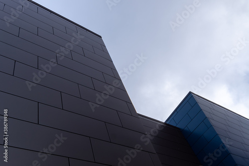 Beige and blue exterior walls of a modern aluminum business building with oblong metal composite panels. The office skyscraper is on a diagonal under a blue sky with thick white clouds.