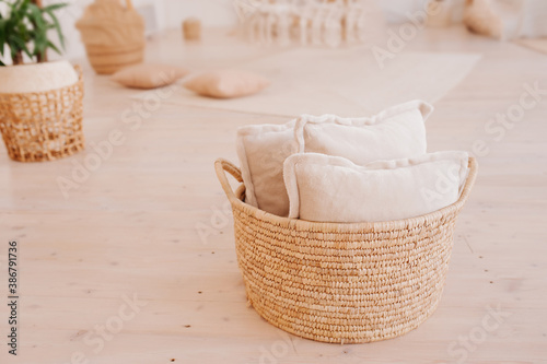 soft light pillows in wide wicker basket on floor of room in minimalistic Scandinavian style. Cozy convenient storage system at home