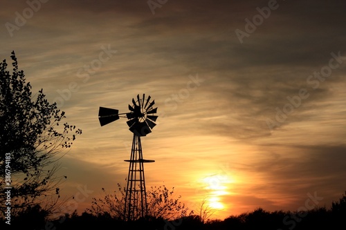 Kansas Windmill silhouette at Sunset with clouds and Sun out in the country north of Hutchinson Kansas USA on a farm.