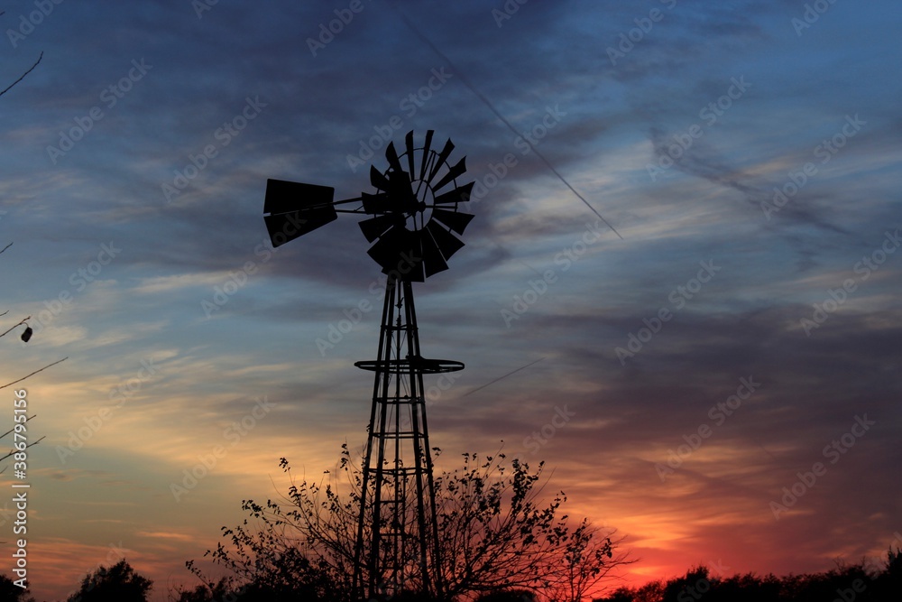 Kansas Windmill silhouette at Sunset with clouds and Sun out in the country north of Hutchinson Kansas USA on a farm. Kansas Windmill silhouette at Sunset with clouds and Sun out in the country north of Hutchinson Kansas USA on a farm.