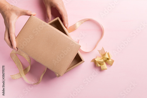 Fototapeta Naklejka Na Ścianę i Meble -  Paper gift box with golden ribbon open by hand on pink background, Present for giving in special day, Top view