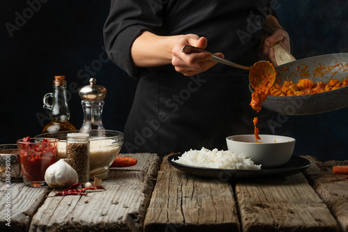 Fotografie Close-up view of chef pours by ladle chicken curry from pan wok to white bowl