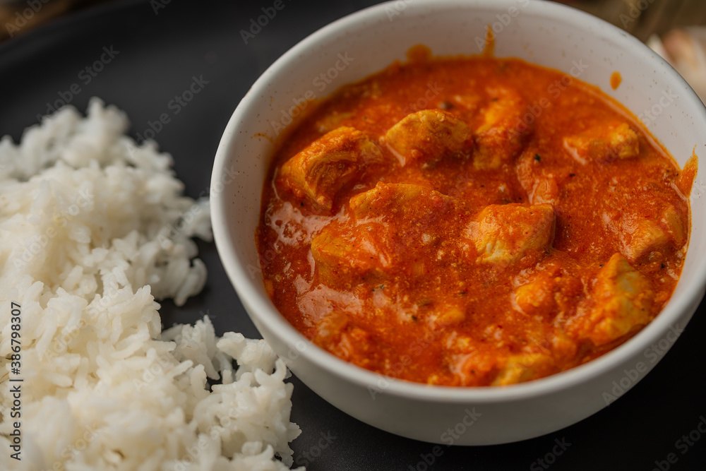 Close up view of appetizing butter chicken curry dish from classic Indian cuisine. Black round plate background. Exotic spicy dish. Horizontal format.