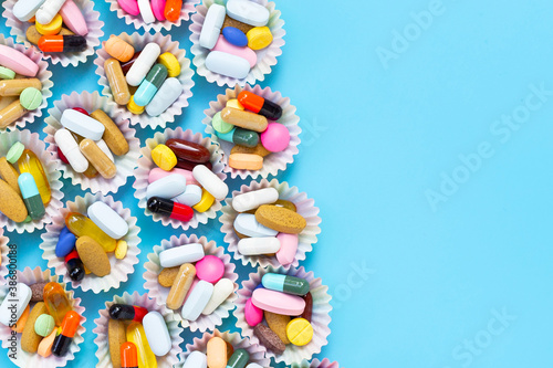 Colorful tablets with capsules and pills in cupcake wrappers on blue background.