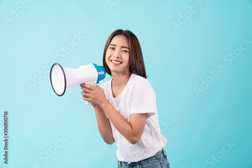 Young Asian woman standing on a blue background and hand touches on mouth with yelled for something.