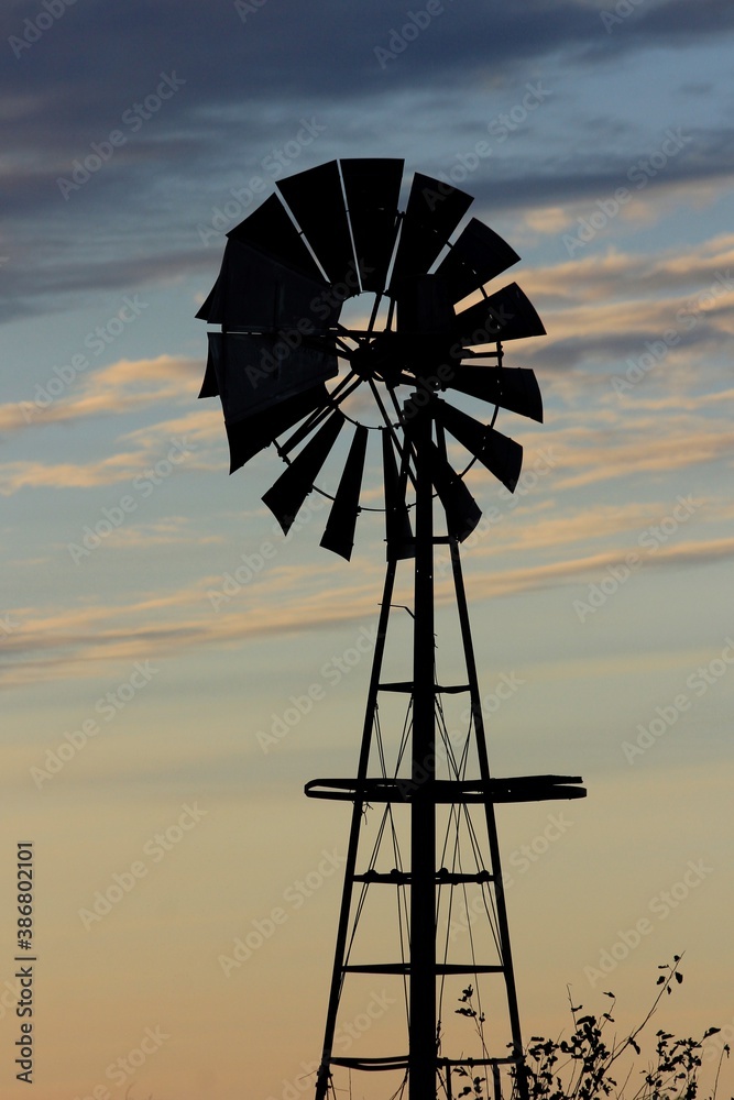 Kansas Windmill silhouette at Sunset with clouds and Sun out in the country north of Hutchinson Kansas USA on a farm. Kansas Windmill silhouette at Sunset with clouds and Sun out in the country north of Hutchinson Kansas USA on a farm.