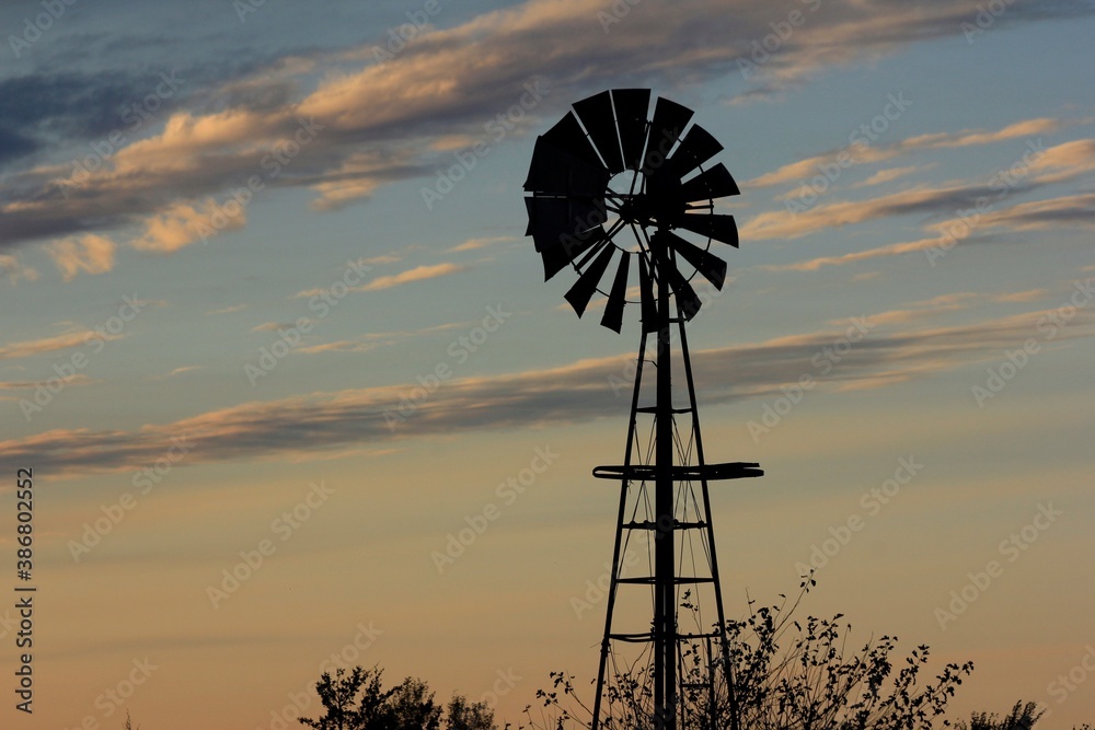 Kansas Windmill silhouette at Sunset with clouds and Sun out in the country north of Hutchinson Kansas USA on a farm. Kansas Windmill silhouette at Sunset with clouds and Sun out in the country north of Hutchinson Kansas USA on a farm.