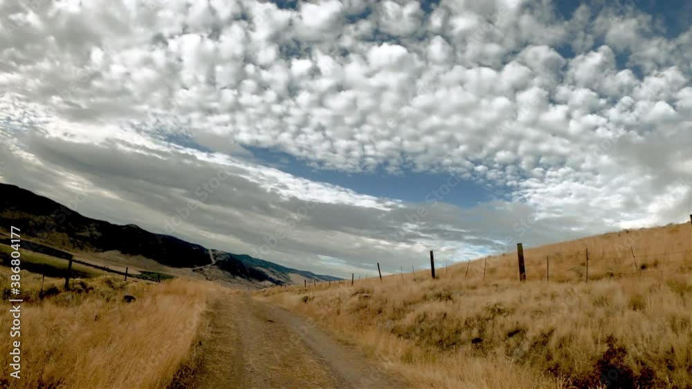 Driving along a winding path between hills covered with yellow grass on a sunny autumn day. Silhouettes of mountains and blue sky with white clouds on the horizon. Driving along a winding path between hills covered with yellow grass on a sunny autumn day. Silhouettes of mountains and blue sky with white clouds on the horizon.