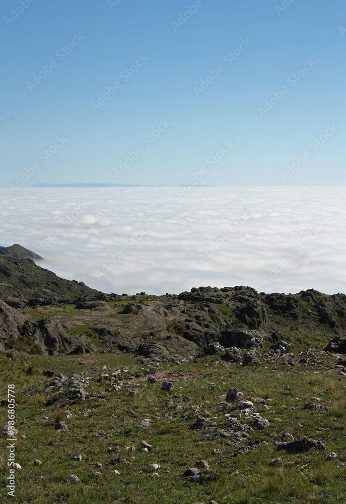 Above the sea of clouds. Beautiful view of the green meadow and white clouds, from the top of the hill.