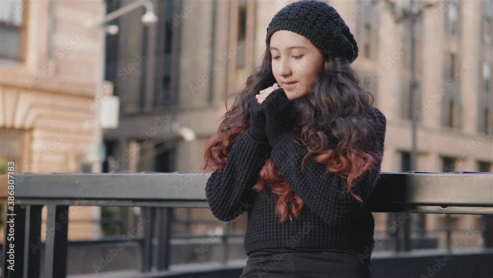 Vista de una niña adolescente por las calles de la Ciudad de México con ropa de abrigo en una tarde de otoño, niña se frota las manos porque tiene frio, imagen urbana con una chica recargada