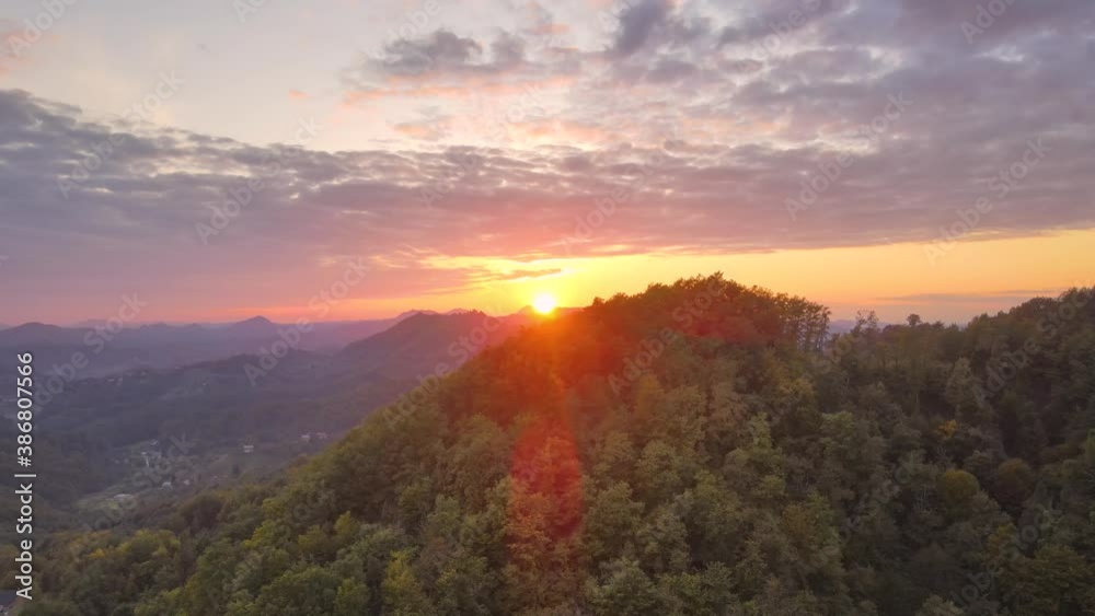 Aerial view over dense green mountains with sun setting below in horizon in background, under a dramatic sky. Sliding left. Aerial view over dense green mountains with sun setting below in horizon in background, under a dramatic sky. Sliding left.