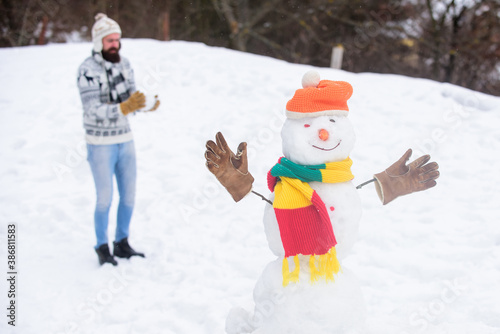 Snowman and cheerful bearded hipster knitted hat and warm gloves play with snow outdoors. Have fun winter day. Let it snow. Christmas holidays. Active lifestyle. Snow games. Leisure on fresh air