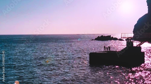 three children run and jump together into sea from pier at sunset. Zoom in