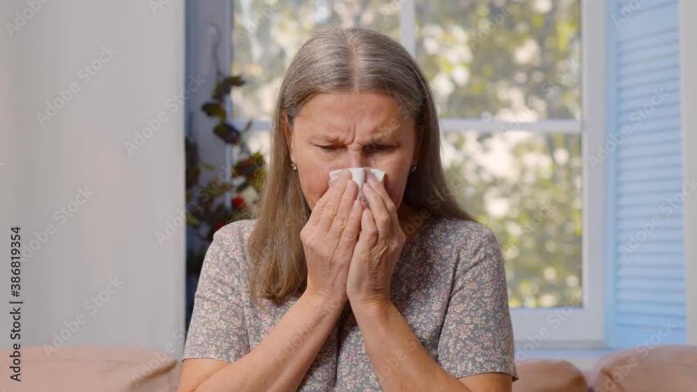 Ill mature woman blowing running nose sitting on couch Ill mature woman blowing running nose sitting on couch