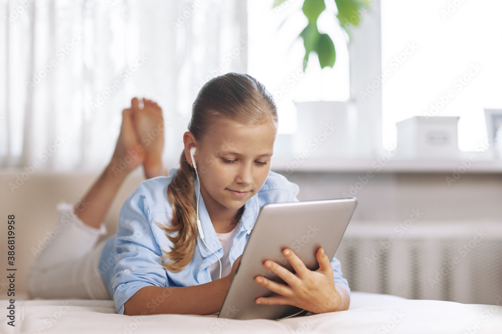 Blonde teenage girl lying on the couch plays a game on the tablet and communicates via video link with friends. Digital technologies Blonde teenage girl lying on the couch plays a game on the tablet and communicates via video link with friends. Digital technologies