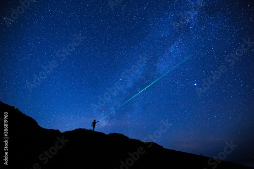 Silhouette of girl / woman standing on the hill use a laser pointer to point at a star. Stargazing at Oahu island, Hawaii. Starry night sky, Milky Way galaxy astrophotography.