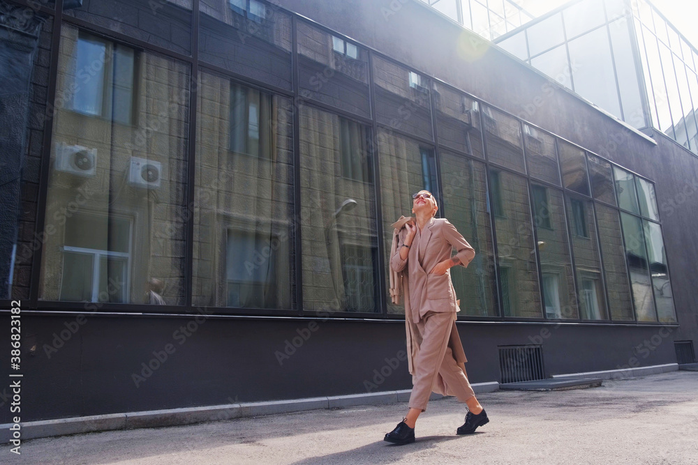 A woman with short hair in gray coat and glasses dancing, walking, smiling on a city street. A woman with short hair in gray coat and glasses dancing, walking, smiling on a city street.